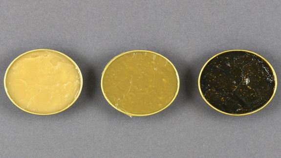 tres contenedores circulares en fila llenos de grasas industriales en amarillo brillante a la izquierda, amarillo oscuro en el centro y negro a la derecha